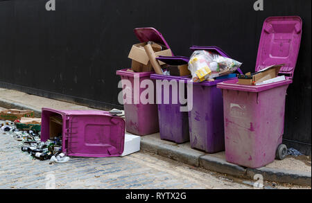 Lila und rosa Mülleimer überlaufen und Glasflaschen auf dem Boden aus einem Fach auf die Seite. Stockfoto