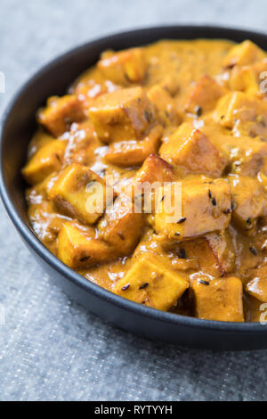 Cremige paneer Curry. Glänzend Hüttenkäse curry mit Gewürzen. Würfel von Paneer in einer dicken, cremigen Sauce Curry in einem schwarzen Schüssel in gezoomt. Grauer Hintergrund Stockfoto