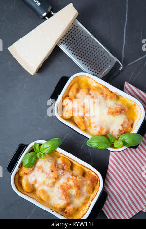 Gnocchi alla Sorrentina in zwei Pasta Gerichte Backen auf einem dunklen Küche oben und pamesan Käse und einer Reibe im Hintergrund. Gebackene gourmet Gnocchi mit m Stockfoto