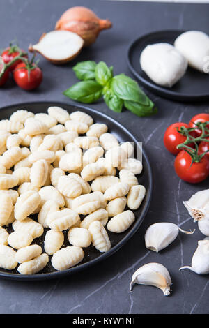 Frische italienische Zutaten. Gebackenen gnocchi alla sorrentina Zutaten. Frischen Gnocchi auf schwarzem Teller mit frischen italienischen Produkten im Hintergrund. Gr Stockfoto