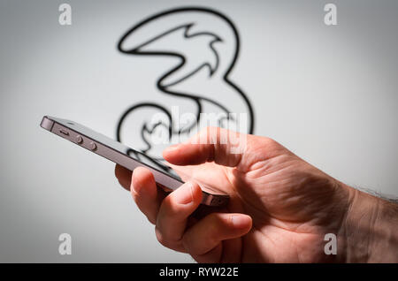 Ein Mann mit einem Handy vor den drei Mobile Network Logo Stockfoto
