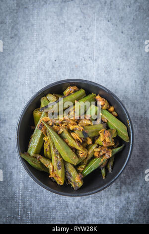 Vegetarische okra Curry in einem kleinen schwarzen Schüssel Schuß mit einer Ansicht von oben. Indische Fried Okra Curry in der Mitte. Bhindi curry mit einem grauen Hintergrund. Stockfoto