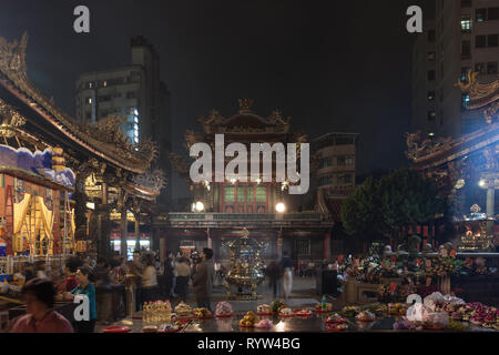 Lungshan Tempel, historischen buddhistischen und taoistischen Tempel, Anbeter, Essen und Blumen Angebote bei Nacht gesehen, Wanhua District, Taipei City, Taiwan Stockfoto