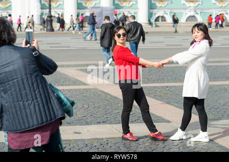 Junge Frauen aus asiatischen Aussehen werden auf dem Schlossplatz vor dem Hintergrund der Eremitage in St. Petersburg, Russland, September, 2018 fotografiert. Stockfoto