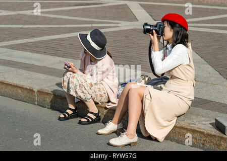 Eine junge Frau und ein Mädchen der Östlichen Aussehen in hellen Pastelltönen Kleidung und Hüte, sitzt auf dem Bürgersteig, Bilder der Sehenswürdigkeiten der Palace s nehmen Stockfoto