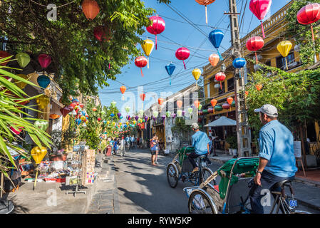 Hoi An, Vietnam - Oktober 24, 2018: zwei rikschas fahren Sie entlang einer bunten Straße in der Altstadt von Laternen dekoriert. Stockfoto