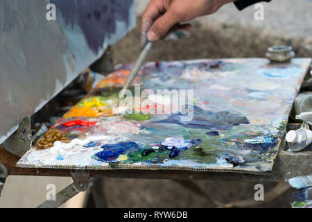 Artist's Staffelei mit einer Palette von hellen Farben. Die Hand des Künstlers ist mit einem Besen der Vermischung malen. Kunststoff bokeh. Stockfoto