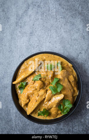 Chicken Korma Curry in der Mitte in einem schwarzen Schüssel und hellgrauen Hintergrund. Runde Schale mit indischen Chicken Korma curry mit frischen Korianderblättern. Stockfoto