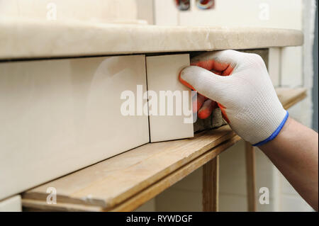 Die Hand des Arbeitnehmers setzt das Stück der Fliese auf der gekrümmten Wand unter einem Waschbecken. Stockfoto