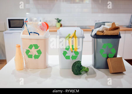 Mülltrennung zu Hause. Die Umwelt zu schützen. Bunte Mülltonnen mit Recycling Symbol voller Kunststoff-, Lebensmittel-, Papier auf dem Tisch close-up Stockfoto