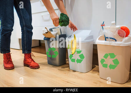 Mülltrennung zu Hause. 7/8-Ansicht von Frau, Brokkoli in der Mülltonne. Bunte Mülleimer für die Sortierung der Abfälle in der Küche Stockfoto