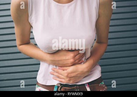 Junge Frau mit den Händen auf Magen schlecht Schmerzen Schmerzen isoliert auf grauem Hintergrund. Lebensmittelvergiftung, Grippe, Krämpfe. Fragen Probleme Gesundheitskonzept Stockfoto