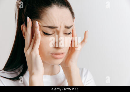 Frau mit Kopfschmerzen. Auf grauem Hintergrund. Geschäftsfrau mit Schmerzen auf grauem Hintergrund. Weibliches Brustbild. Menschliche Gefühle, Mimik Konzept. Stockfoto