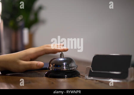 Close up Frauen rufen Sie das Hotel an der Rezeption auf dem Schreibtisch mit dem Finger drücken Sie eine Glocke in der Lobby Hotel. hotel Konzept. Stockfoto