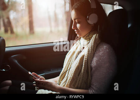 Frau im Auto, Herbst Konzept. Lächelnd hübsche Mädchen, das Hören von Musik über Kopfhörer im Auto Stockfoto