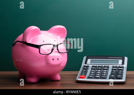 Taschenrechner und rosa Sparschwein mit Brille Vor der grünen Platine Stockfoto