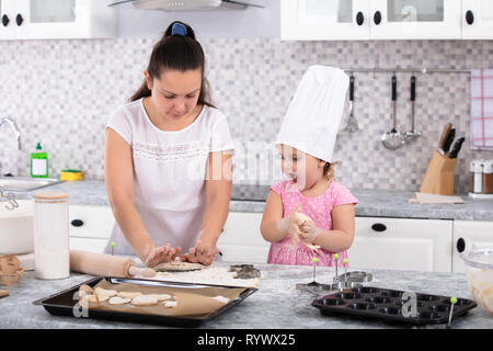 Mädchen mit Küchenchef hat zu helfen, ihre Mutter zu Cookies an Küche Stockfoto