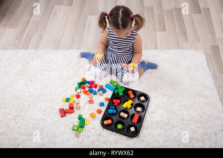 Ansicht von Mädchen sitzen auf dem Teppich Spielen mit bunten Bausteinen zu Hause Stockfoto