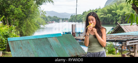 Junge asiatische Mädchen essen Bananen mit Fluss im Hintergrund Stockfoto