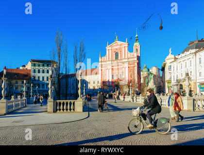 Ljubljana, Slowenien - 14 Januar, 2019: Frau auf Fahrrad an der Franziskanerkirche und Triple Brücke über Fluss Ljubljanica Straßen der Altstadt in Ljubljana, Slowenien. Türme der Kathedrale und die slowenische Stadt Stockfoto