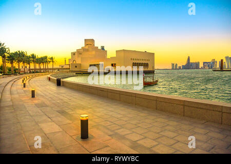 Seafront Laufsteg mit Palmen entlang der Bucht von Doha mit Dhow und Wolkenkratzer von Doha West Bay Skyline bei Sonnenuntergang. Urbane Stadtbild. Die katarischen Hauptstadt in Stockfoto