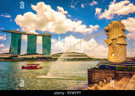 Singapur, Singapur - 1. März 2016: Merlion statue spritzt das Wasser aus dem Mund am Merlion Park an der Marina Bay in Singapur. Marina Bay Sands Hotel und Fähre auf dem Hintergrund. Stockfoto