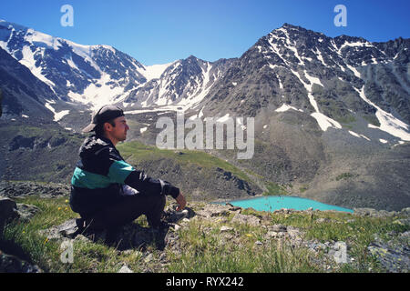 Junge Mann in Schwarz Sportswear sitzt auf der Klippe und suchen Tal unten, Misty. Schönen Hintergrund Landschaft mit hohen Bergen mit s Stockfoto