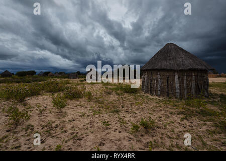 Regen gefüllten dunklen Gewitterwolken Okavanga Dorf überholen mit seinen runden Stroh Häuser und Strohdächern Stockfoto