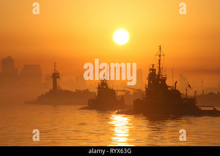 Schlepper vor der Skyline von New York City bei Sonnenaufgang mit der Sonne in einem nebligen Morgen und Orange Sky Stockfoto