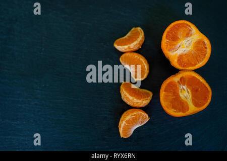 Satsumas/orange/Clementine schließen bis auf dunklem Schiefer Hintergrund in der Hälfte Stockfoto