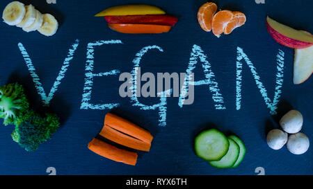 Das Wort vegan in Kreide auf Schiefer, umgeben von Obst und Gemüse geschrieben. Vegane Küche. Veganuary. Werkbasiert Stockfoto