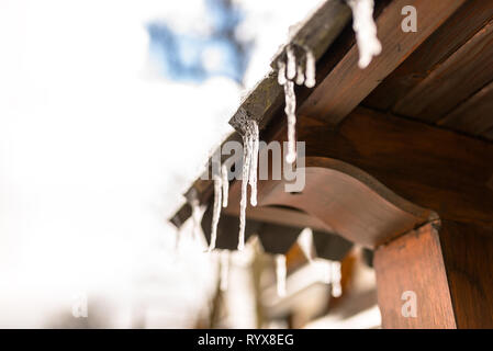 Hängenden Eiszapfen vom Dach eines hölzernen Gebäude auf einem Winter frostigen Tag, viel Schnee auf dem Dach. Stockfoto