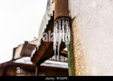 Gefrorenes Wasser vom Dach durch eine beschädigte, rostig, Metall Rinne, die auf der Fassade des Gebäudes ist. Stockfoto