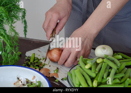 Frische Bohnen über Holz Hintergrund, selektive konzentrieren. Frau ist Hacken von Zwiebeln für das Kochen auf dem Hintergrund Stockfoto