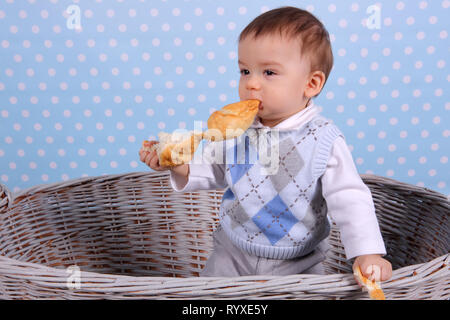 Ein kleines Kind isst ein trockenes Brötchen in einem Korb aus Korbweide Baum gesponnen. Stockfoto