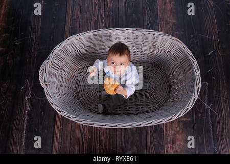 Ein kleines Kind isst ein trockenes Brötchen in einem Korb aus Korbweide Baum gesponnen. Stockfoto