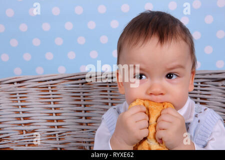 Ein kleines Kind isst ein trockenes Brötchen in einem Korb aus Korbweide Baum gesponnen. Stockfoto