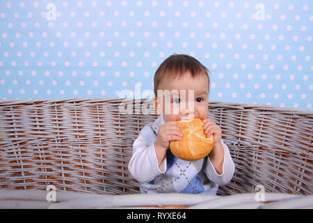 Ein kleines Kind isst ein trockenes Brötchen in einem Korb aus Korbweide Baum gesponnen. Stockfoto