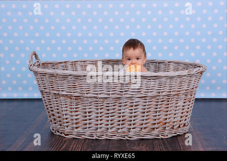 Ein kleines Kind isst ein trockenes Brötchen in einem Korb aus Korbweide Baum gesponnen. Stockfoto