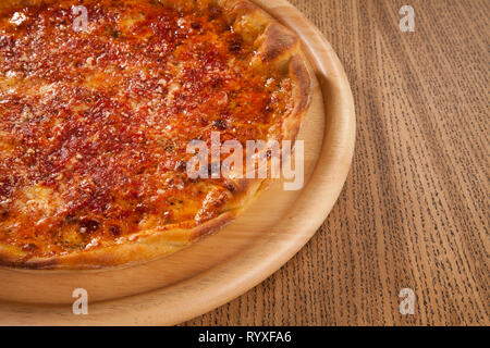 Pizza mit Käse heiß serviert und lecker auf Holzplatte auf Tisch. Schnelle und kostengünstige Mahlzeit Stockfoto