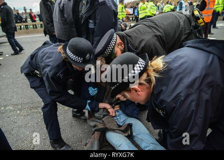 London, Großbritannien. 15 Mär, 2019. Ein Student ist auf die Westminster Bridge nach sich hinzusetzen Protest von Studenten Klimawandel Aktivisten verhaftet. Schülerinnen und Schüler gehen in den Streik in Großbritannien heute fordert mehr Maßnahmen gegen den Klimawandel. Polizisten fordern Sie hier mehrmals, wenn Sie sich hinstellen und ohne fremde Hilfe gehen, Sie dos nicht. Die Offiziere tragen Sie in Richtung zu einem Polizeiwagen. Credit: Claire Doherty/Alamy leben Nachrichten Stockfoto