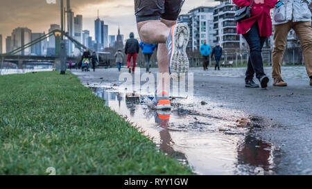 Blick auf die Beine eines Mannes, die nach dem Regen entlang eines Flusses in einer großen Stadt. Frühling Sport Stockfoto