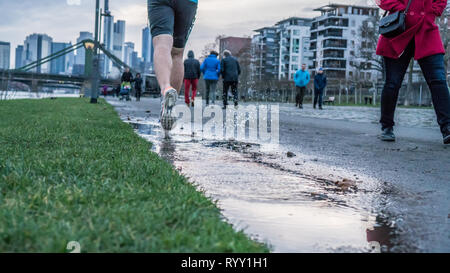 Blick auf die Beine eines Mannes, die nach dem Regen entlang eines Flusses in einer großen Stadt. Frühling Sport Stockfoto