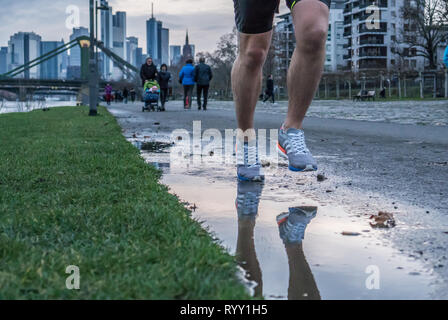 Blick auf die Beine eines Mannes, die nach dem Regen entlang eines Flusses in einer großen Stadt. Frühling Sport Stockfoto