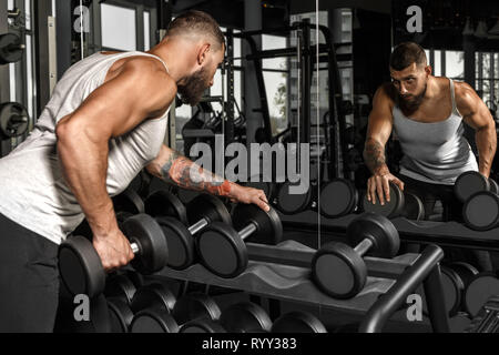 Bodybuilding. Bärtiger Mann trainieren im Fitnessstudio mit Hantel auf Spiegel prüfen Technik Seitenansicht Stockfoto