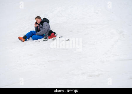 Szklarska Poreba, Polen - Februar 2019: Junge um Hilfe ruft auf seinem Handy nach dem Skifahren oder Snowboarden Unfall auf dem Berghang, Stockfoto