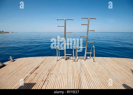 Metall Stahl Leitern auf der Rückseite Teak Deck eines Luxury Motor Yacht segeln auf einem tropischen Meer mit blauem Himmel Hintergrund Stockfoto