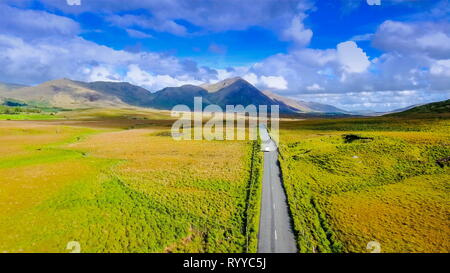 Die lange Straße in der Mitte der Connemara National Park, wo grüne Gräser auf dem Feld sind und die Autos vorbei durch die Straße in Irland Stockfoto