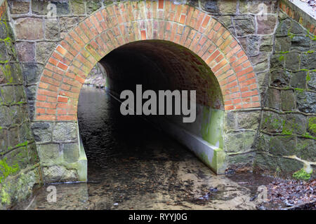 Stein Düker über die Straße für einen kleinen Fluss. Ein kleiner Bach in einem Wald. Saison der Feder. Stockfoto