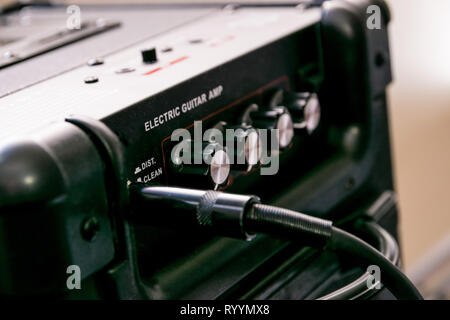 Gitarrenverstärker mit Rädern und Regler für Volume, Gain, Bass, Treble. Jack Kabel angeschlossen. Schwarz Amp mit rotem Licht auf. Stockfoto